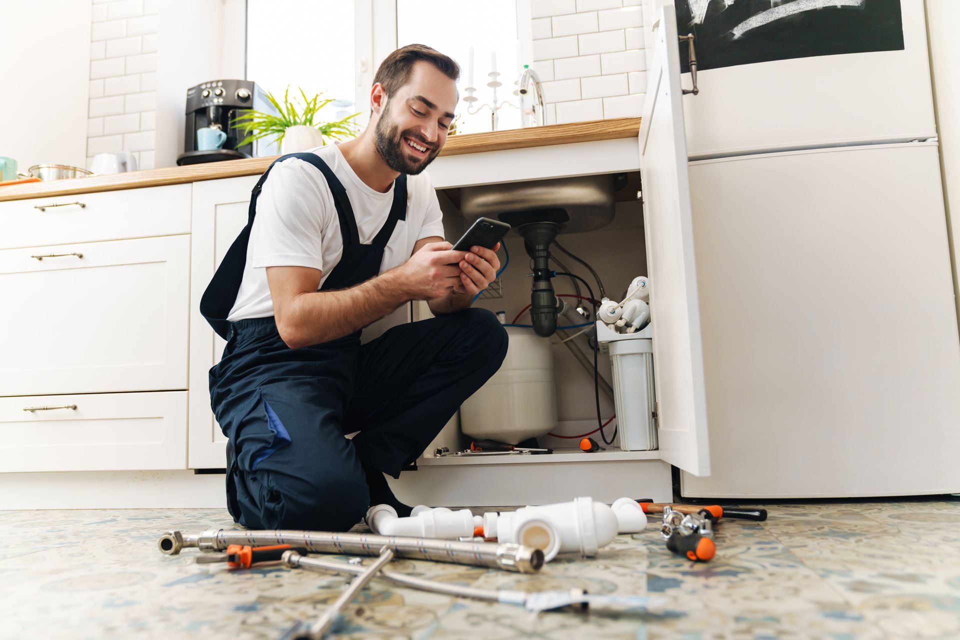 Person kneeling by open sink cabinet checking phone amid plumbing repair. Person kneeling by open sink cabinet checking phone amid plumbing repair.