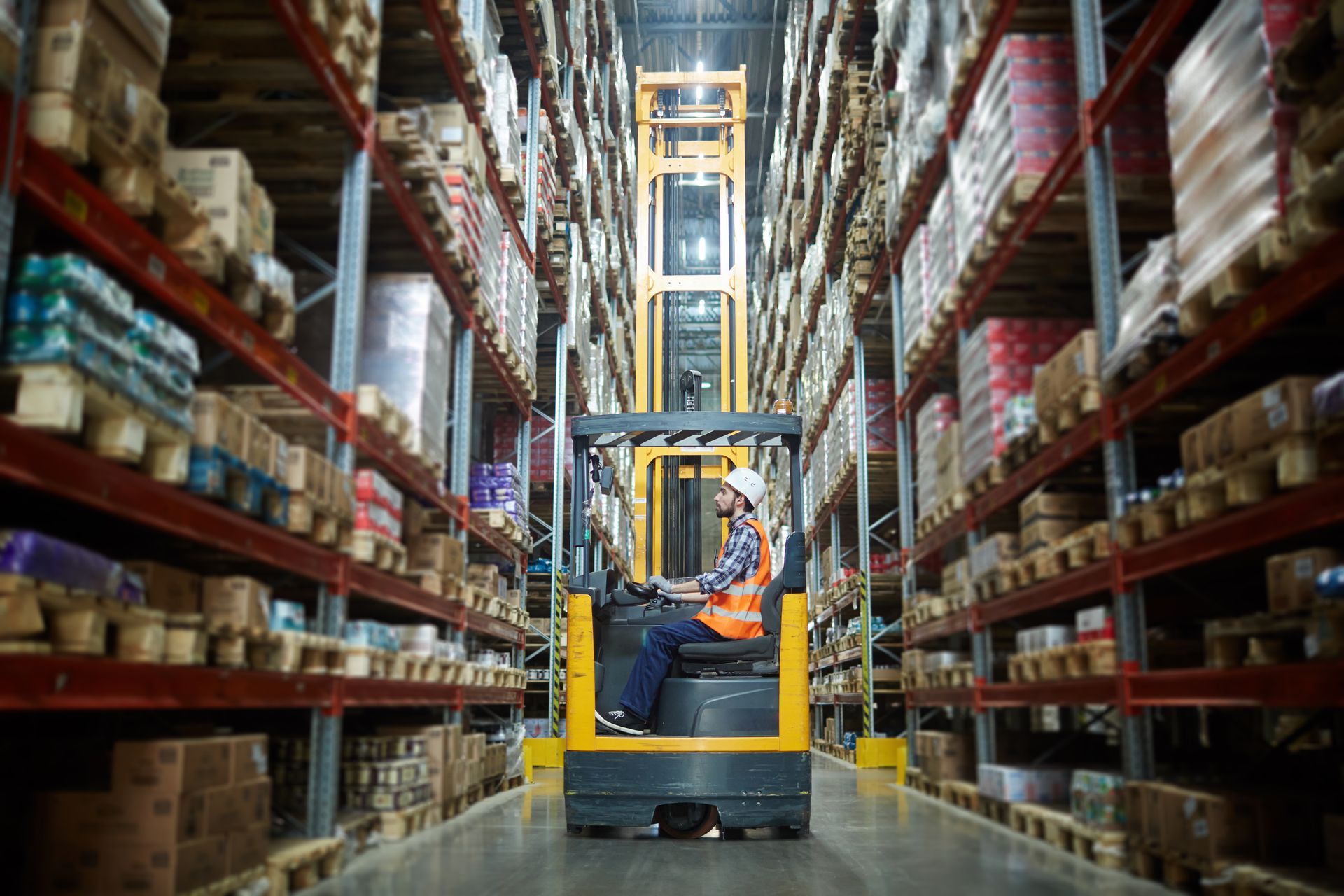 Magazijnmedewerker op een heftruck, die door gangpaden vol dozen en pallets navigeert.