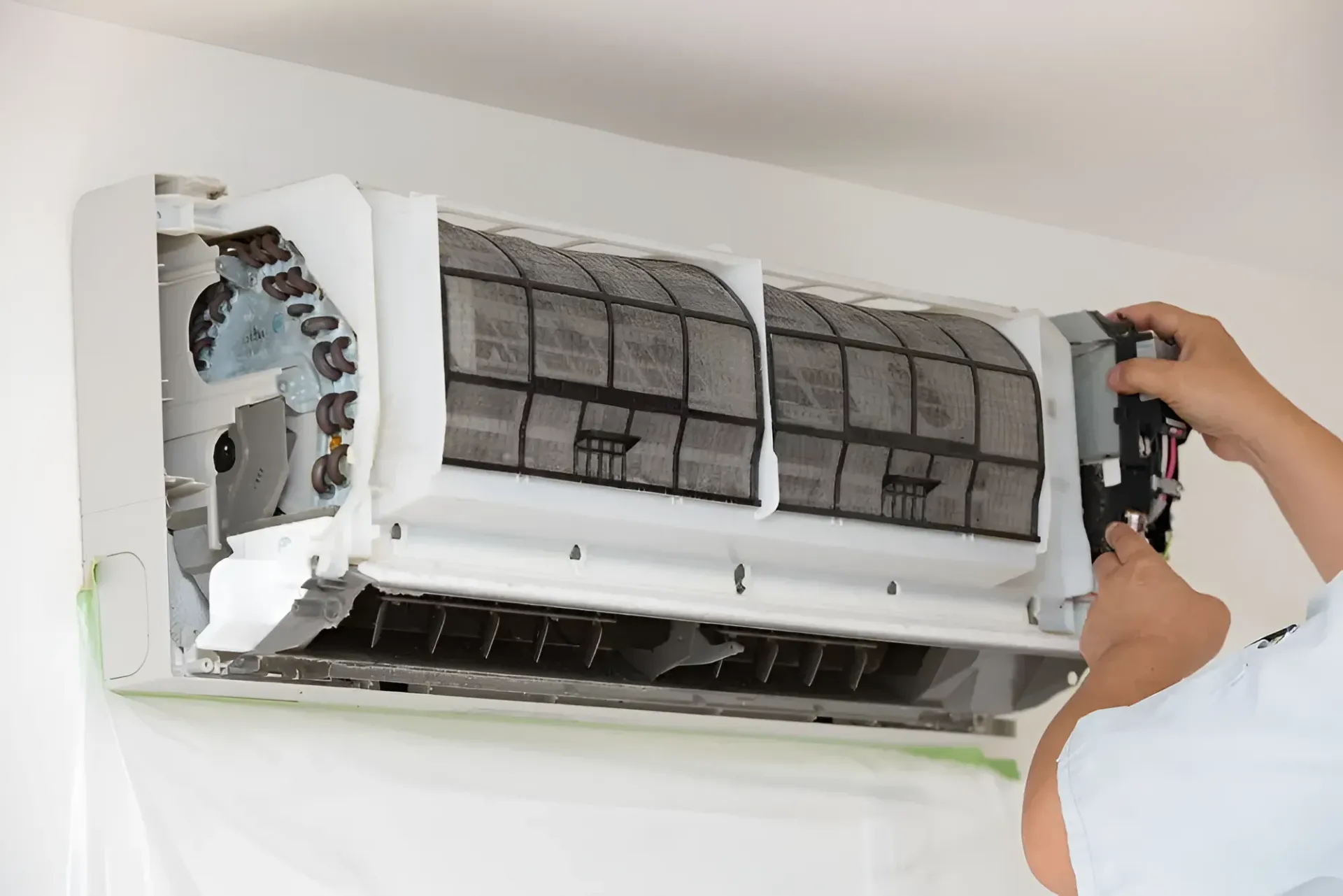Person cleaning air conditioner filter, removing and inspecting it indoors — Chayser Electrical in Currimundi, QLD