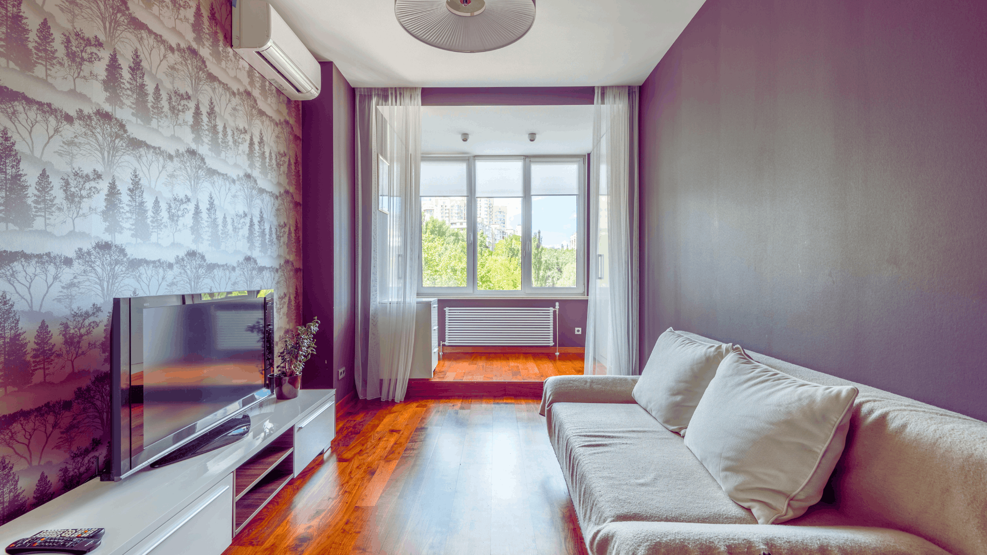 Living room with a gray couch, TV, and balcony. One wall has a forest mural — Chayser Electrical in Currimundi, QLD