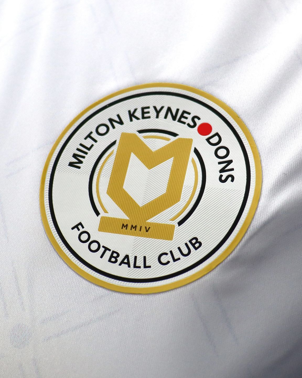 Milton Keynes Dons Football Club logo in black, gold, and white on a shirt