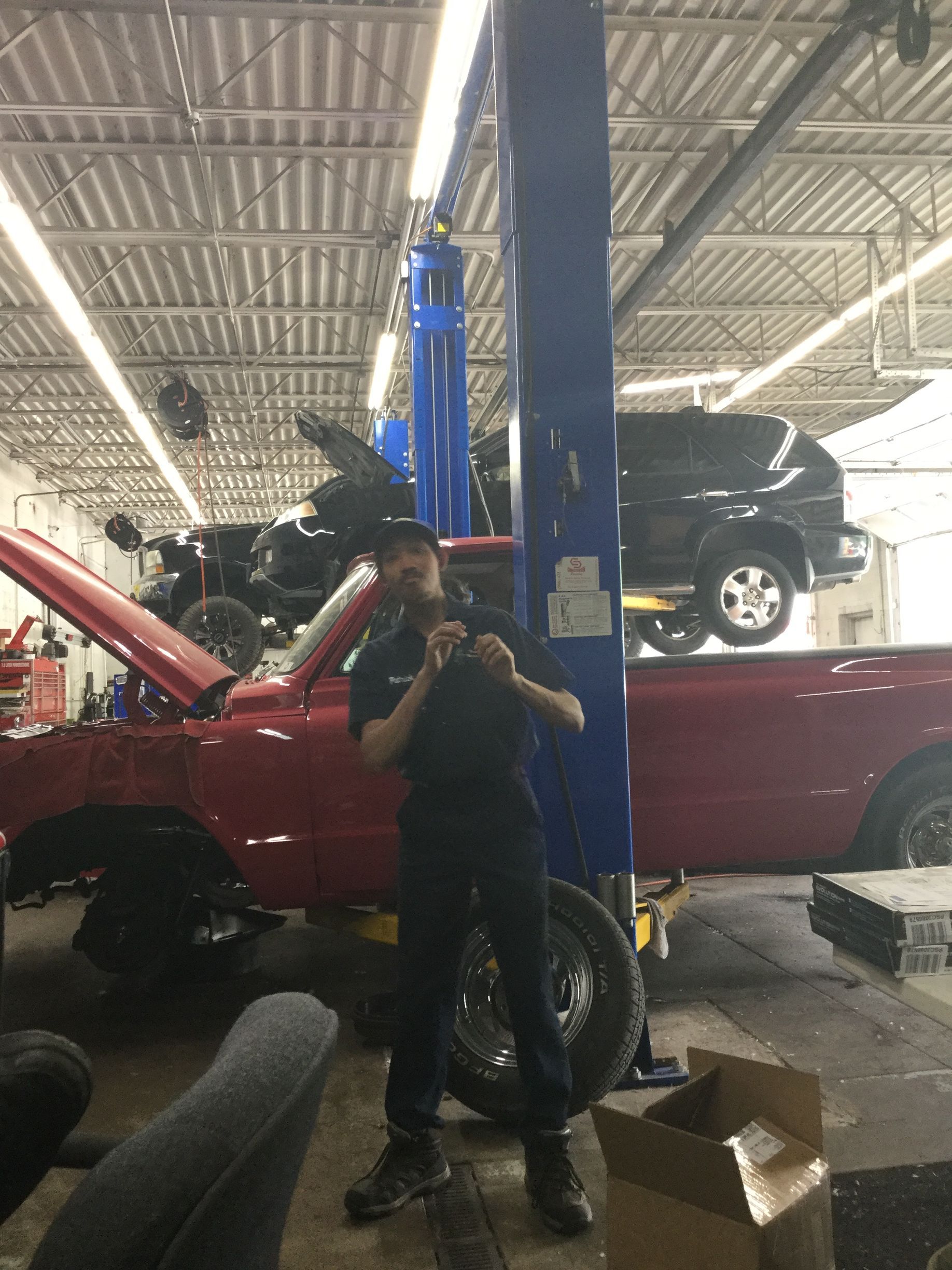 A man is standing in front of a red truck on a lift in a garage.