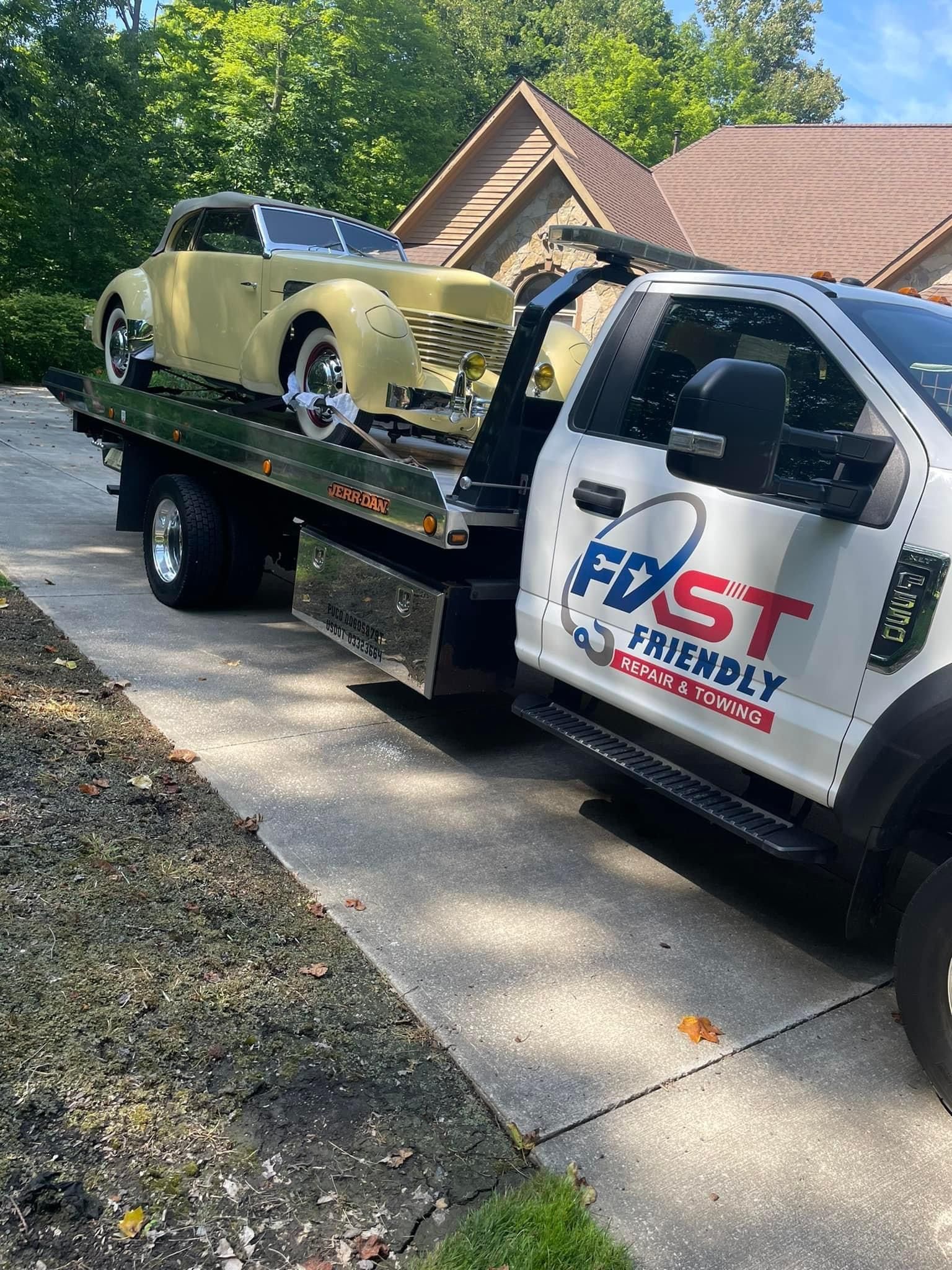 A tow truck is towing a classic car in a driveway.