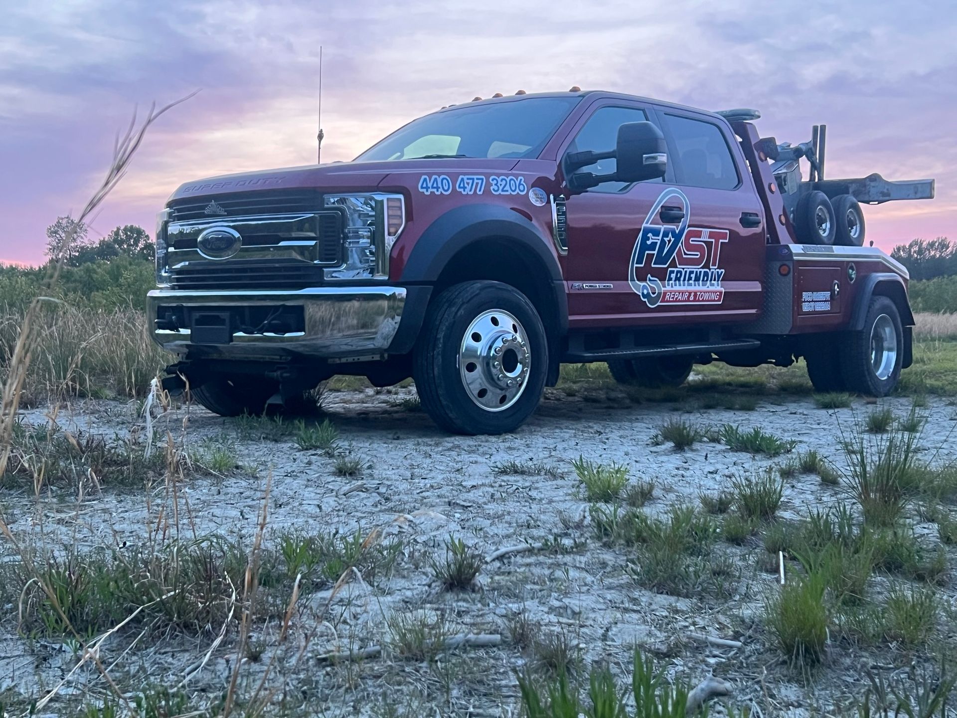A red tow truck is parked in a dirt field.