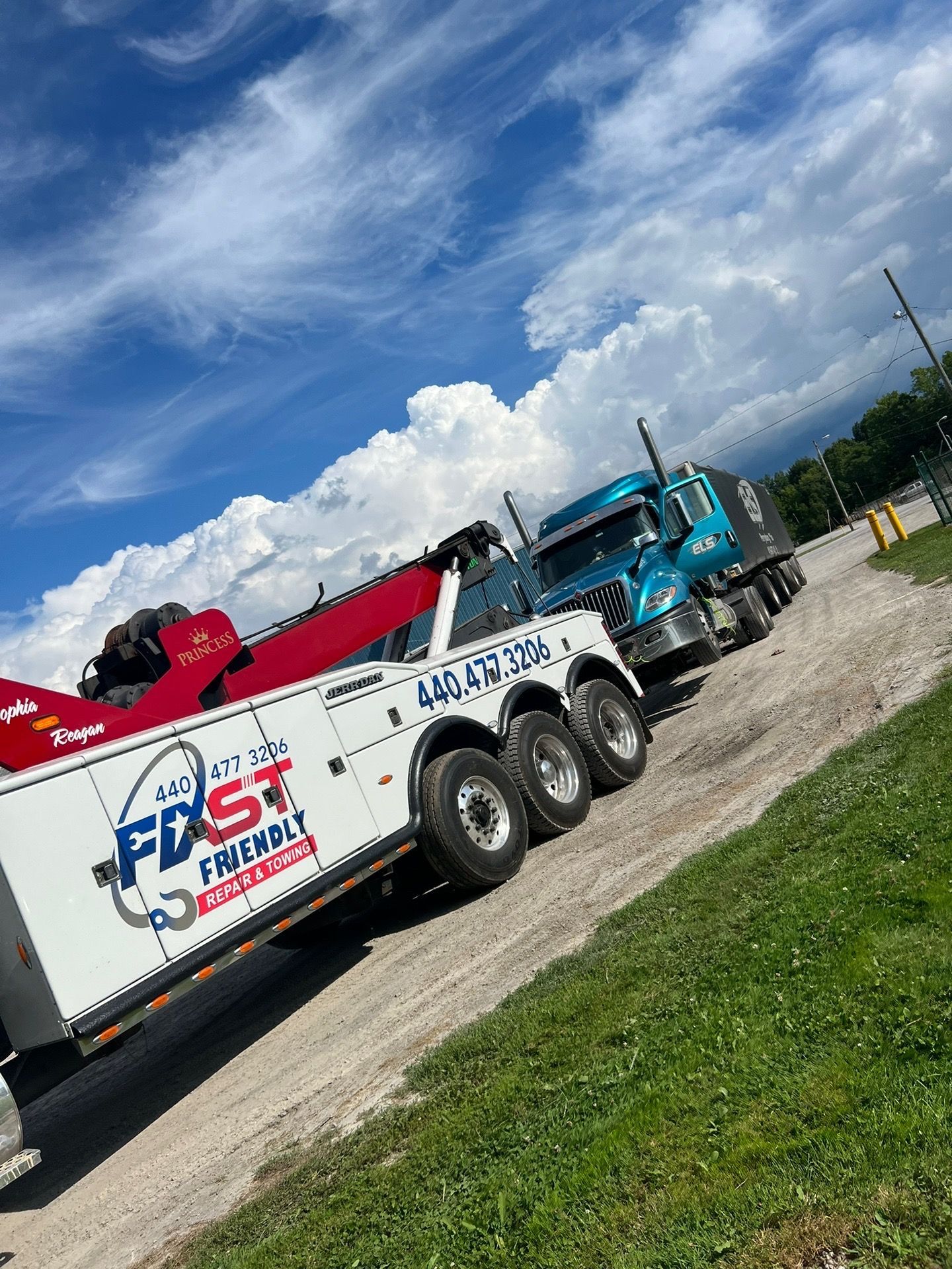 A tow truck is parked next to a semi truck on a dirt road.