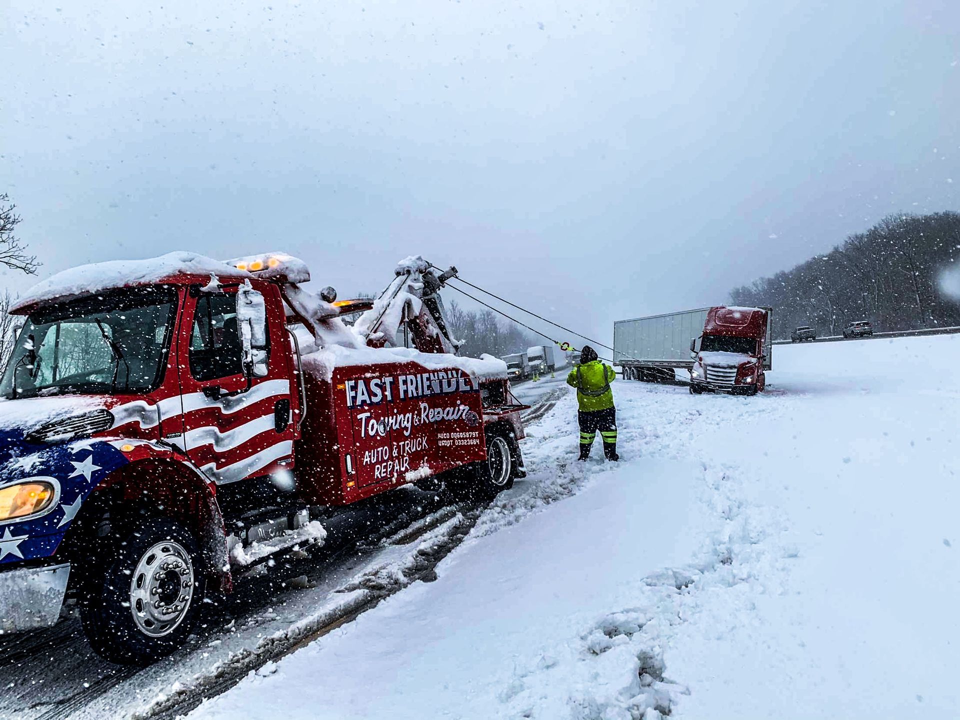 A tow truck is towing a semi truck in the snow.