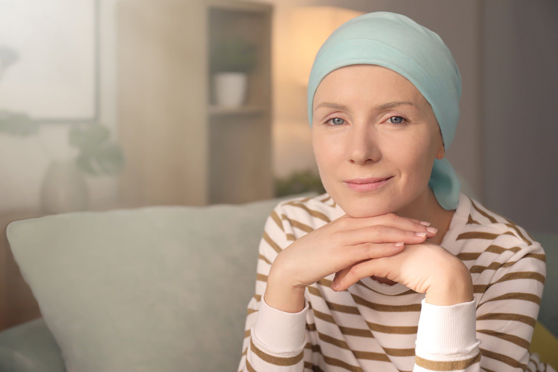 A woman with cancer is sitting on a couch with her hands on her chin.
