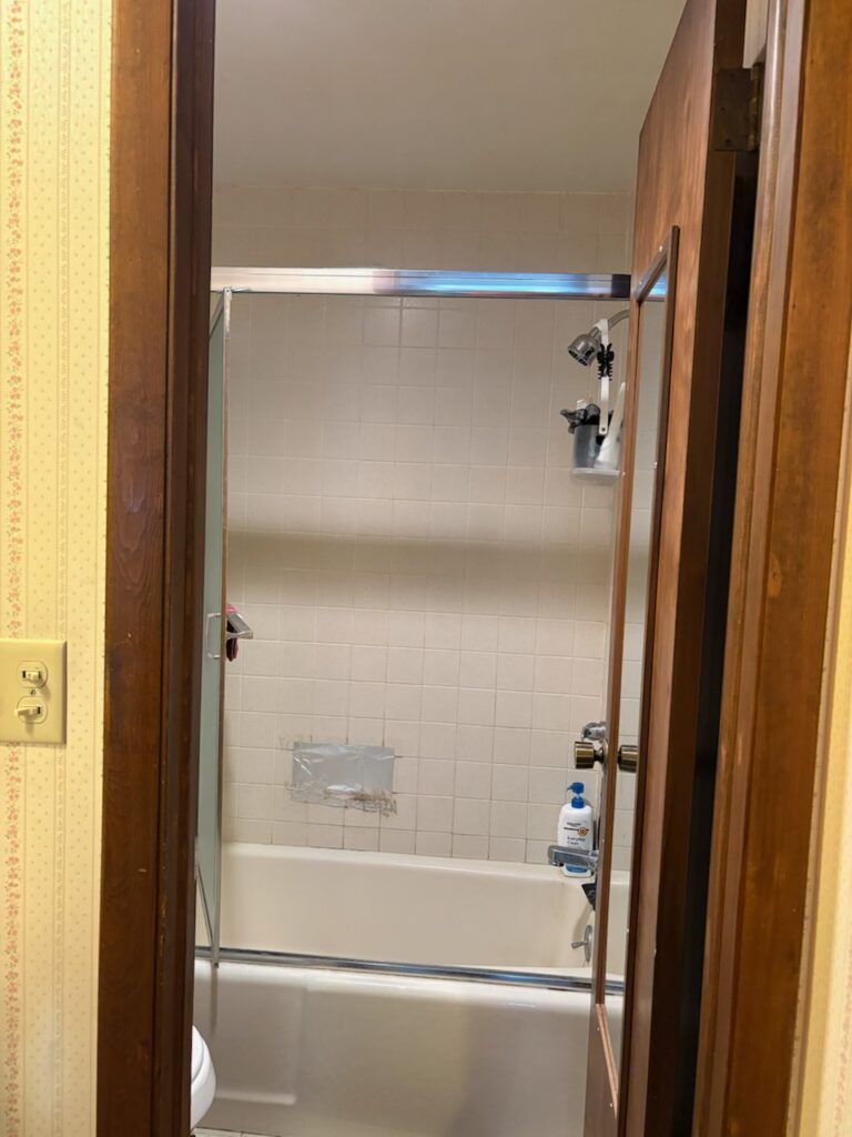 View through a doorway into a small tiled bathroom with a bathtub and shower curtain rod.