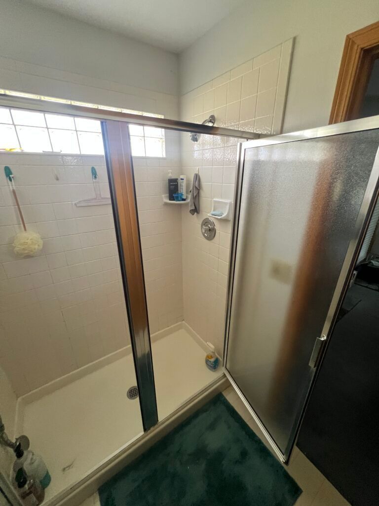 Small bathroom with shower stall, glass doors, tiled walls, and a dark green bath mat