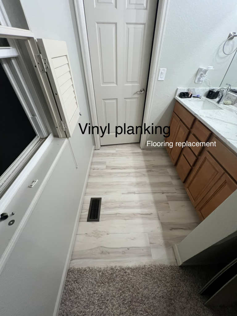 Bathroom floor with light vinyl planking beside vanity and carpet transition.