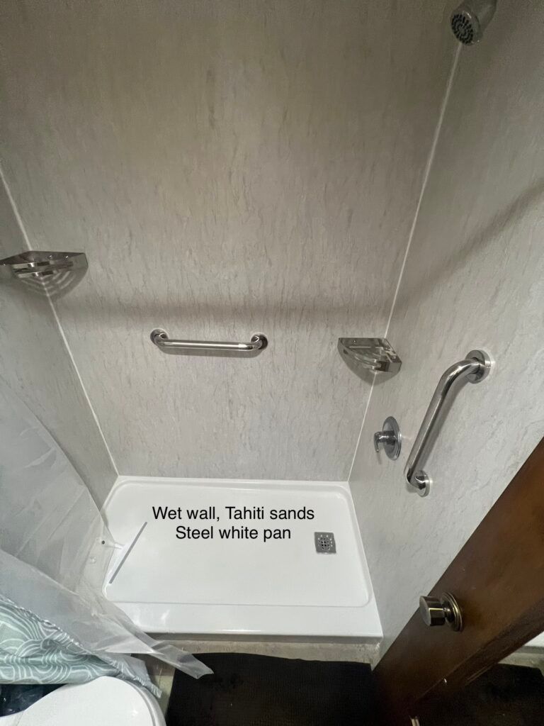 Accessible hotel shower with a fold-down seat, grab bars, and handheld showerhead