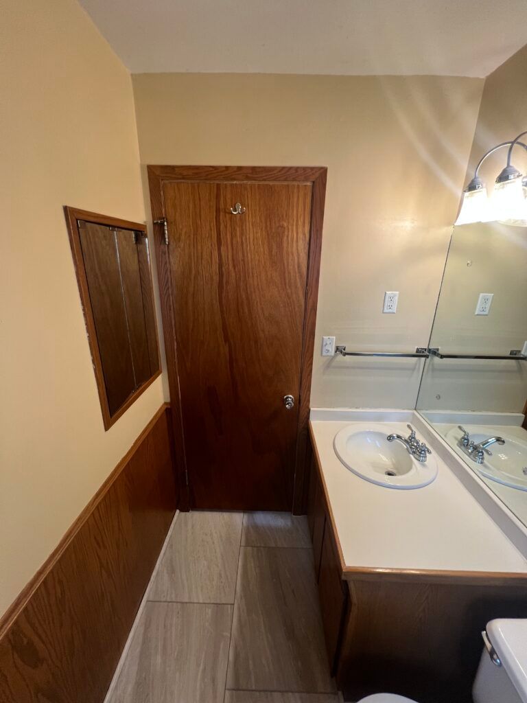Small bathroom with wooden door, sink vanity, mirrored medicine cabinet, and towel bar.