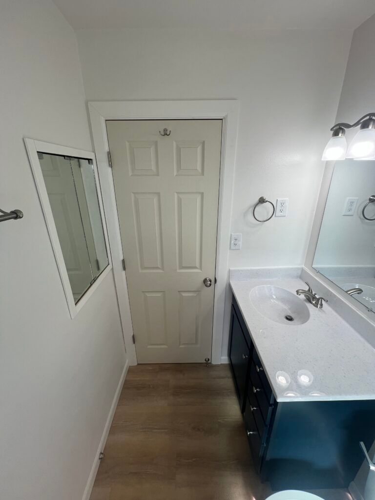 Small bathroom with white walls, beige door, mirrored medicine cabinet, and dark vanity with white countertop.