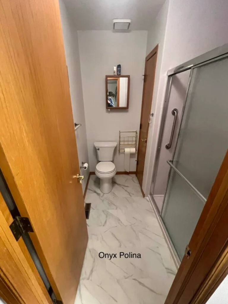 Narrow bathroom with white tile floor, toilet, sink, mirror cabinet, and glass shower door.