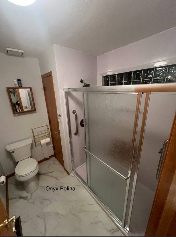Bathroom with toilet, shower stall, and marble-tile floor in a narrow, bright space