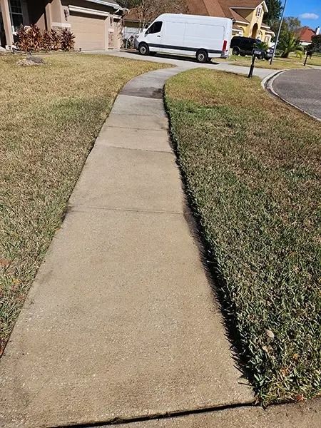 Concrete sidewalk winding through a suburban neighborhood with a white van parked by a house.