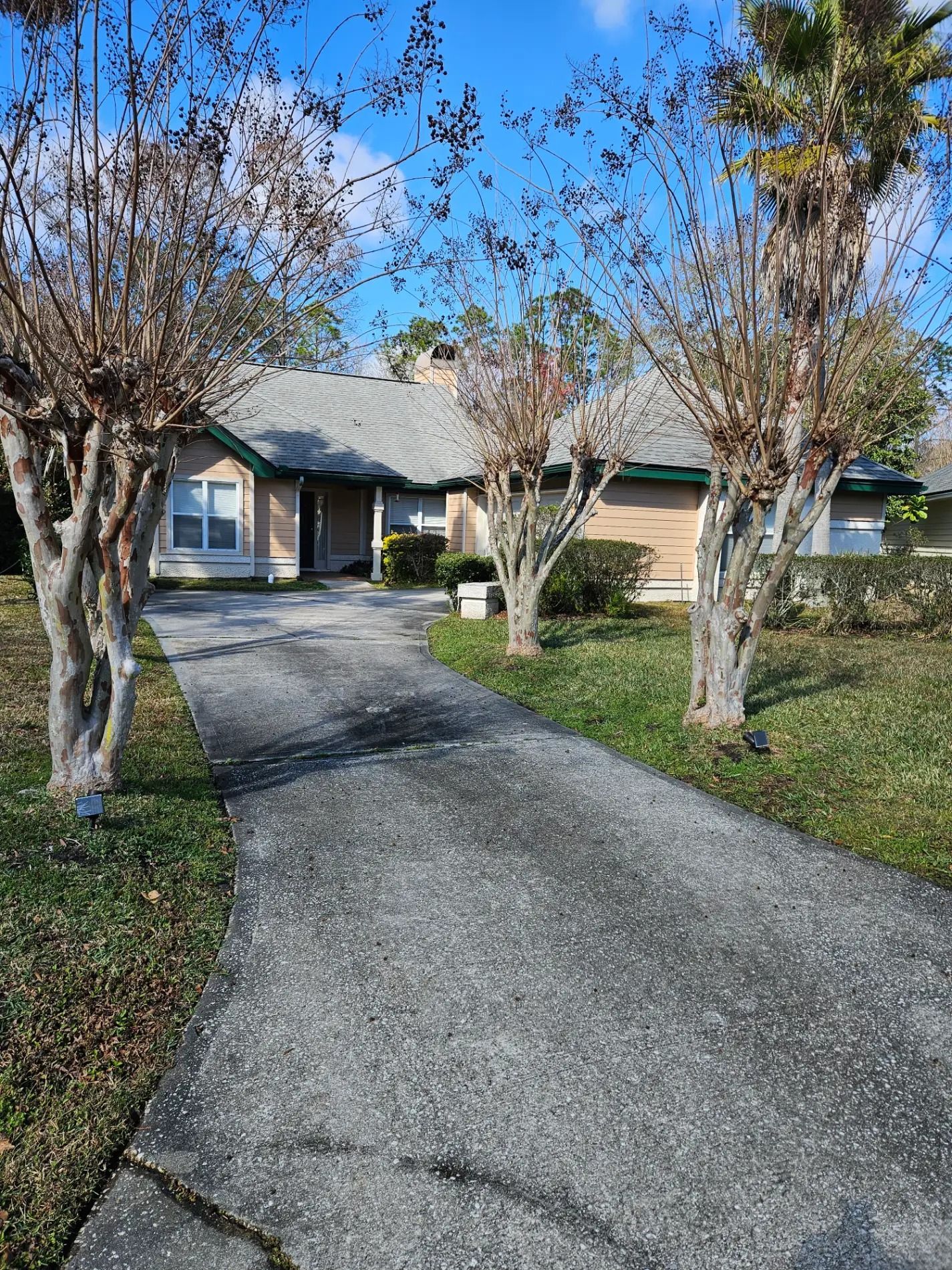 Suburban house with a gravel driveway, bare trees, and clear blue sky