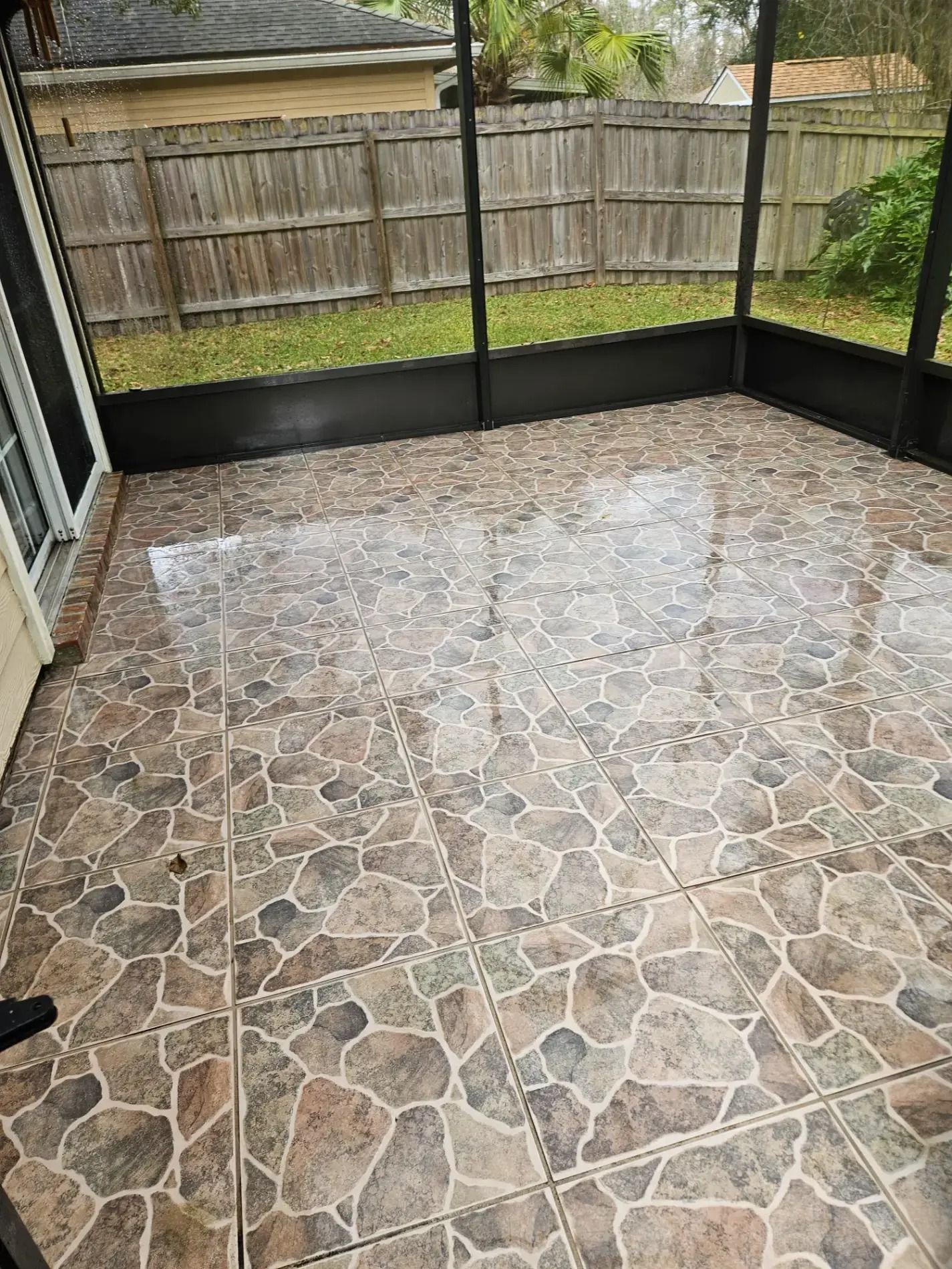 Screened patio with stone tile floor and a wooden fence outside.