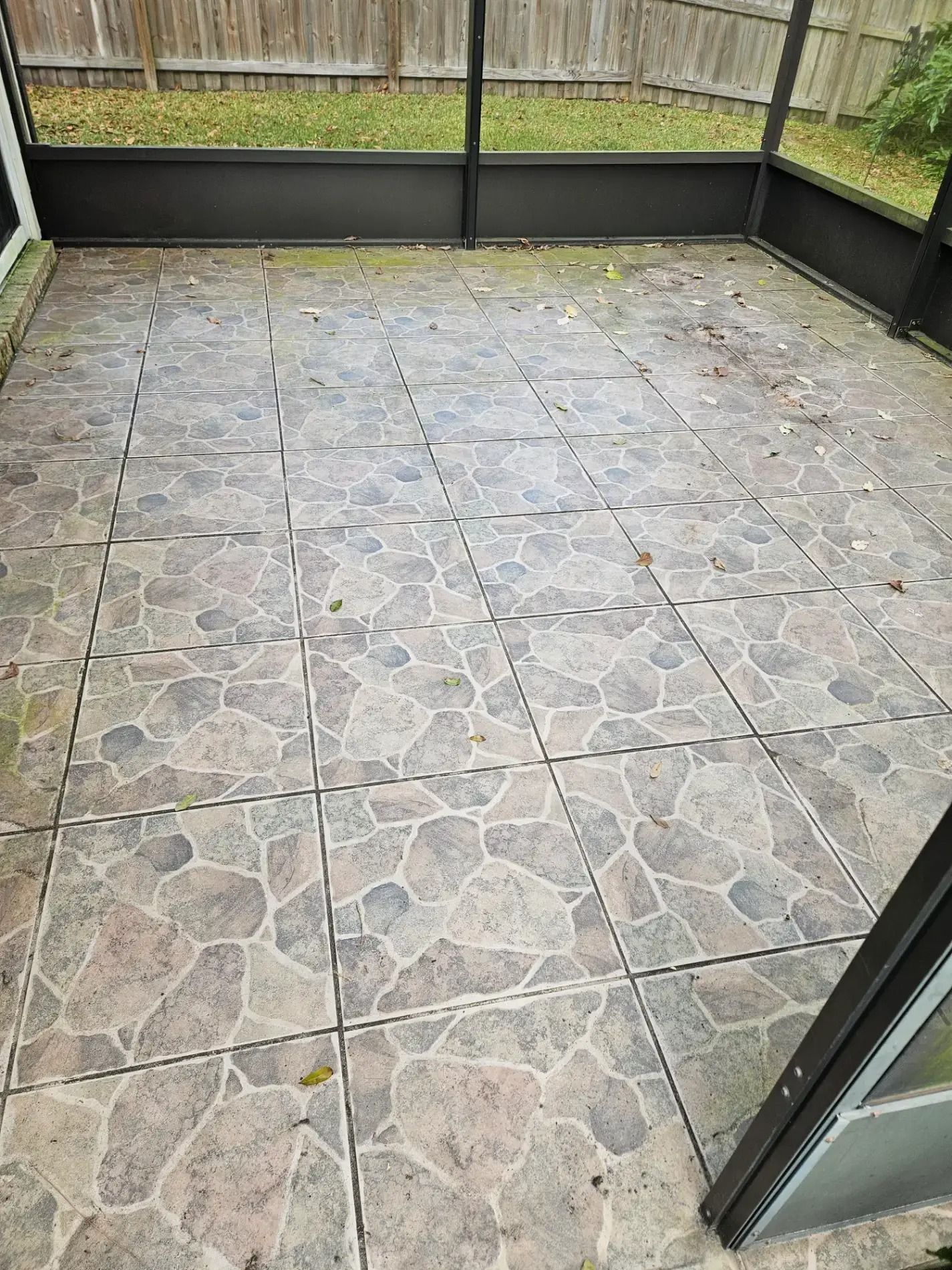 Empty patio with stone-pattern tile flooring and dark gray fencing, viewed from a doorway