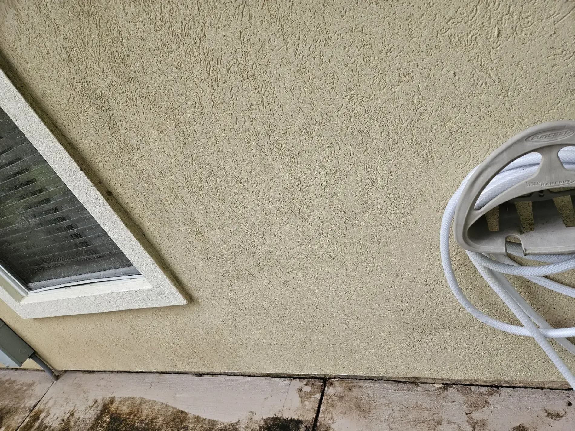 Exterior wall with a vent on the left and a coiled hose reel on the right.