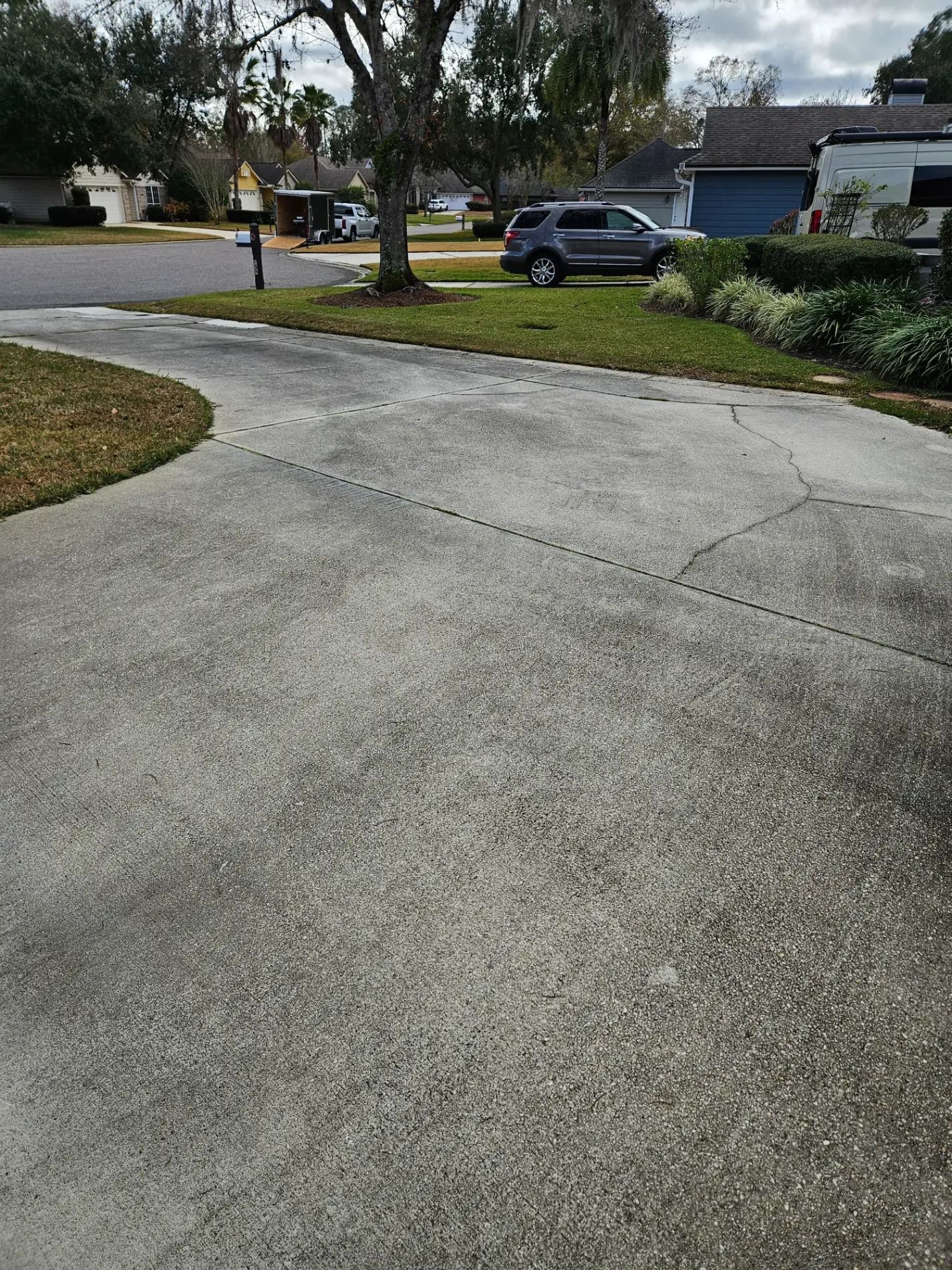 Driveway with a parked gray SUV near a suburban street and houses under cloudy skies