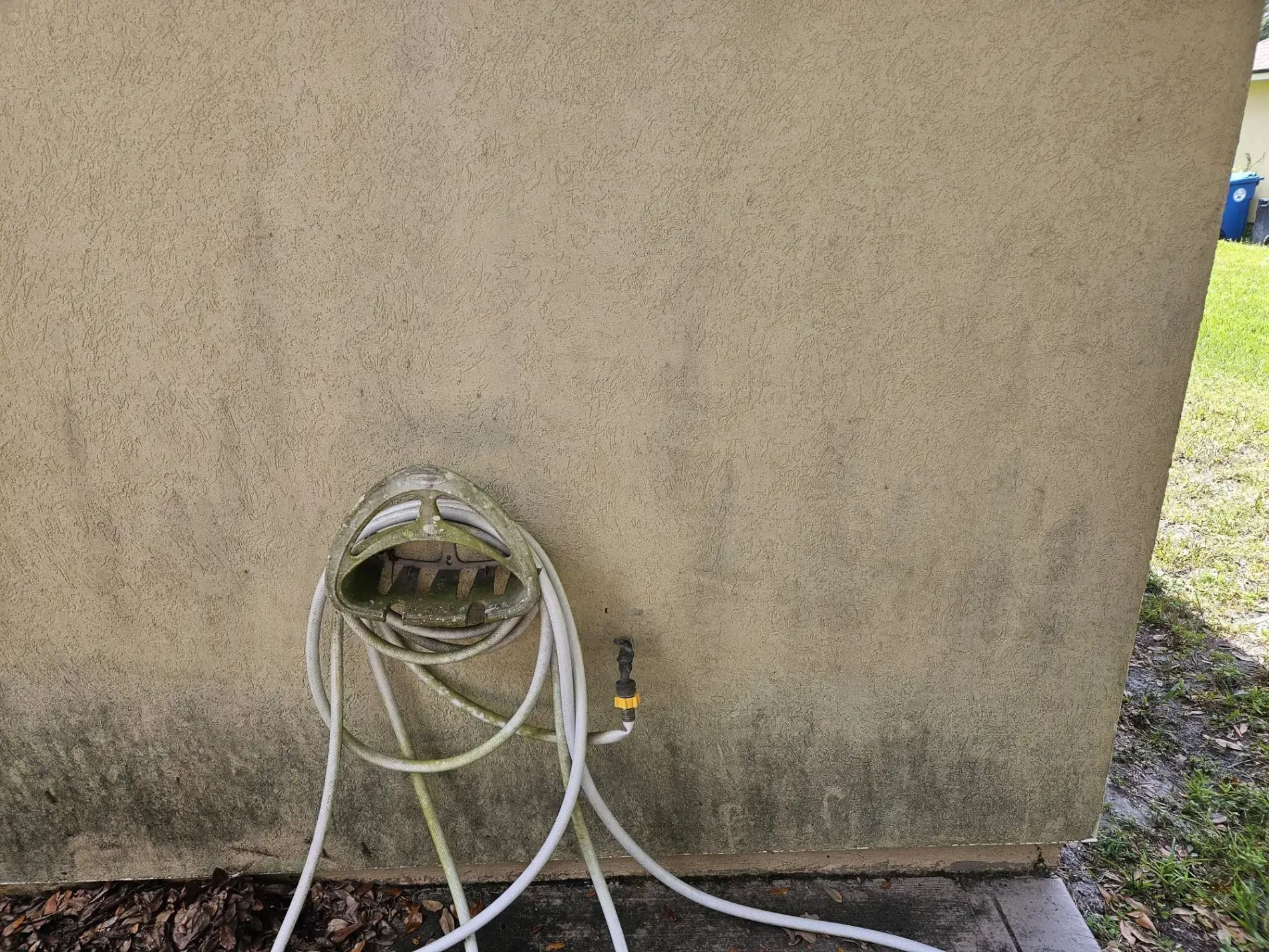White hoses connected to a wall-mounted outdoor faucet on a tan stucco wall.