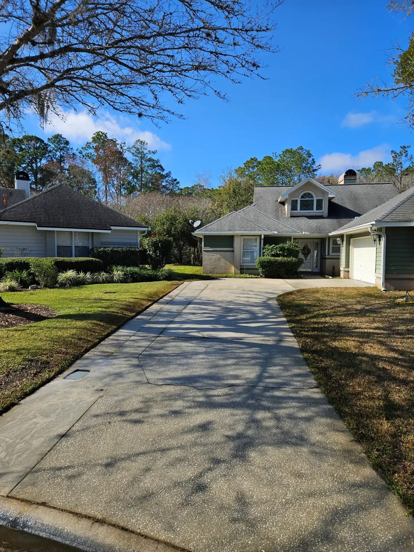 Driveway leading to a suburban house with a garage and dormer windows under a clear blue sky