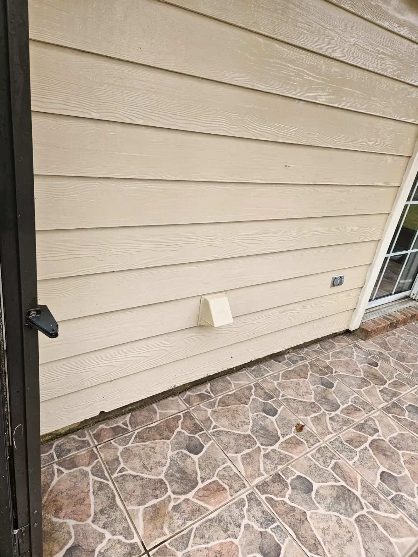 Beige house siding with a small vent and stone patio near a glass door