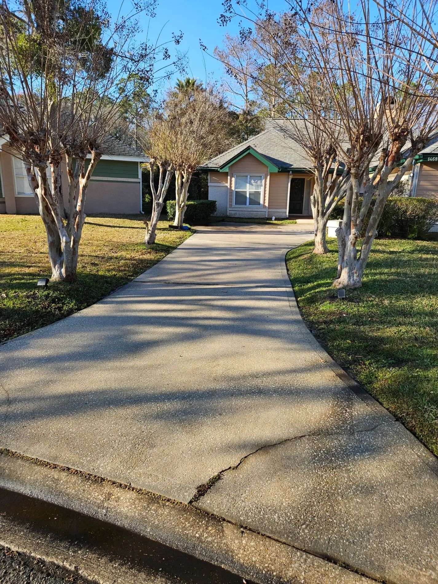 Concrete driveway leading to a small house with a front porch, framed by trees on a sunny day