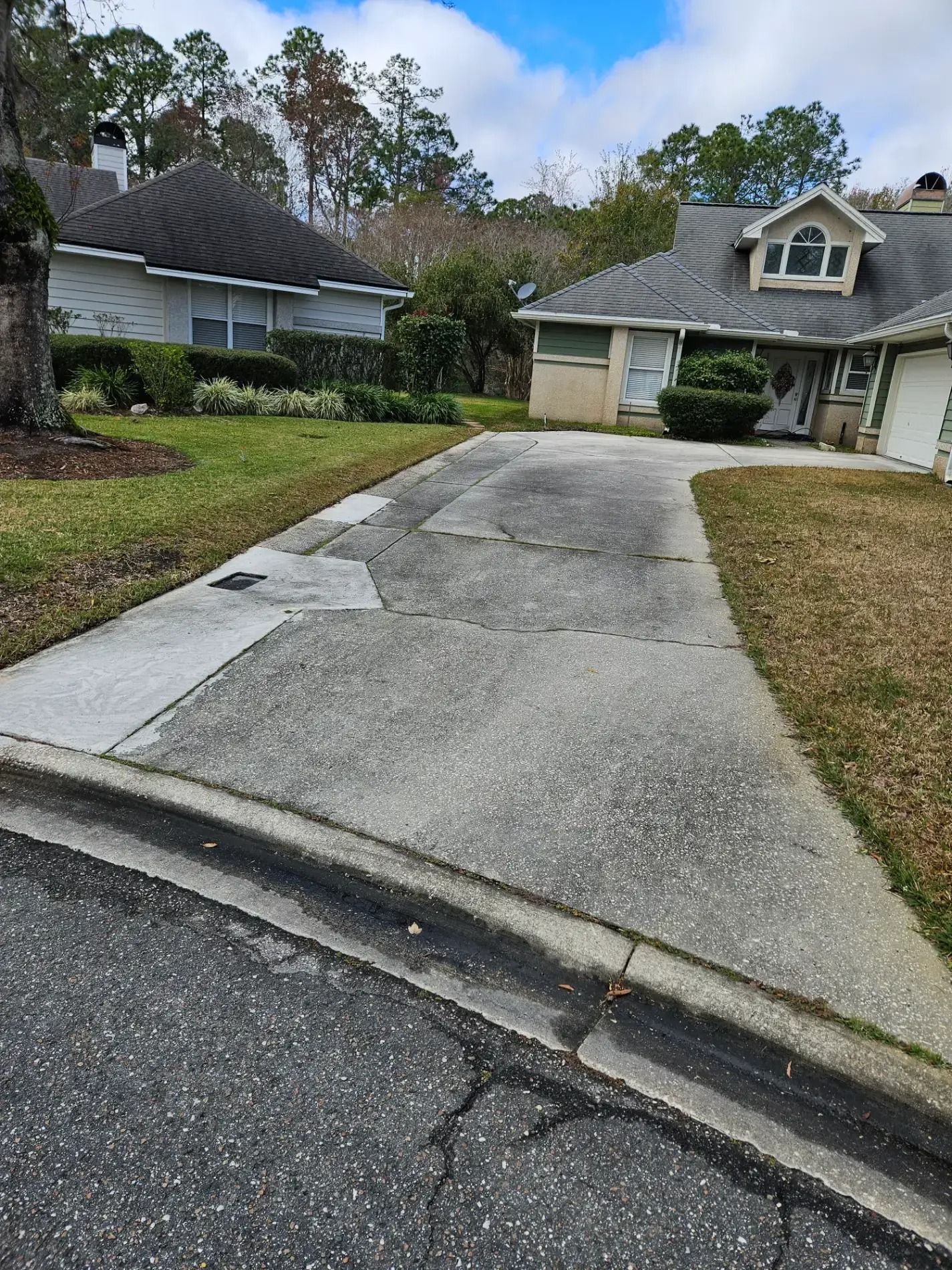 Residential driveway leading to a garage, with a curved curb and neighboring houses on a cloudy day