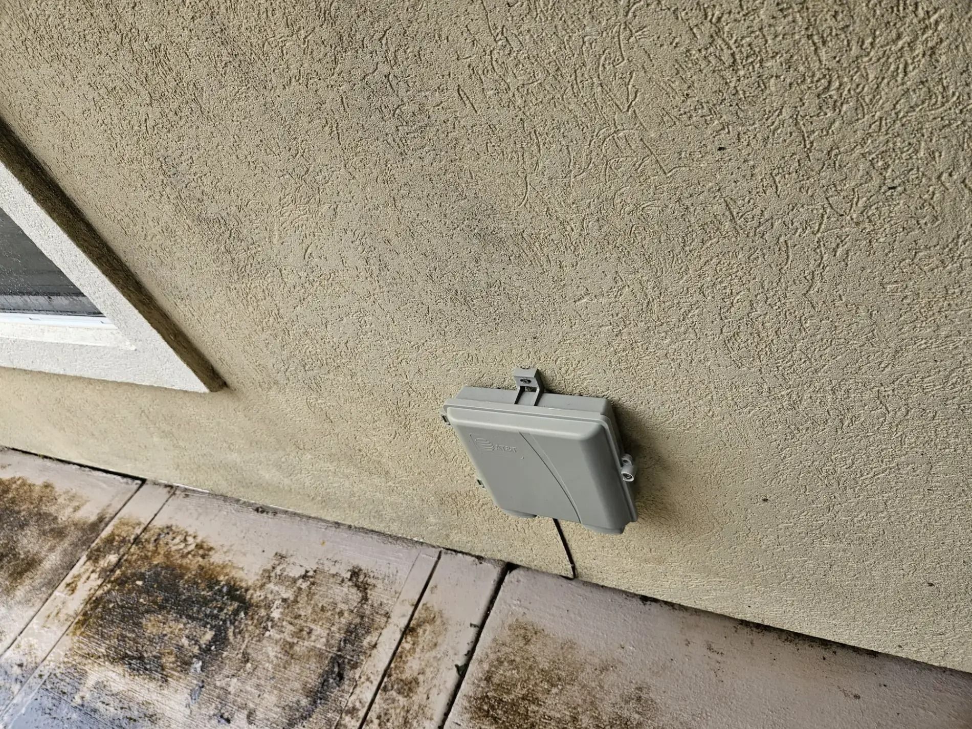 Gray electrical box mounted on a stucco exterior wall beside a concrete walkway