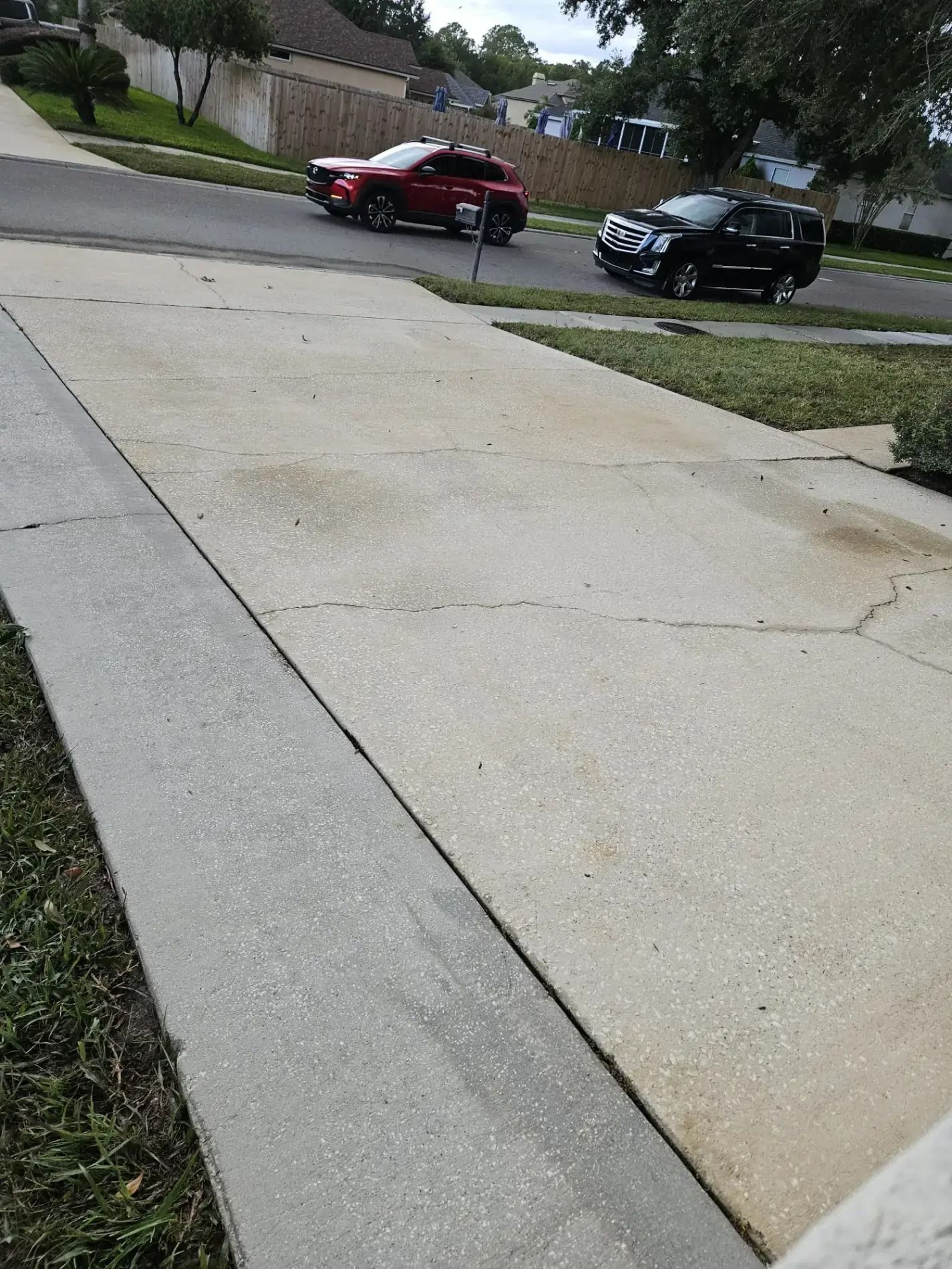Cracked concrete driveway leading to a residential street with two parked cars.