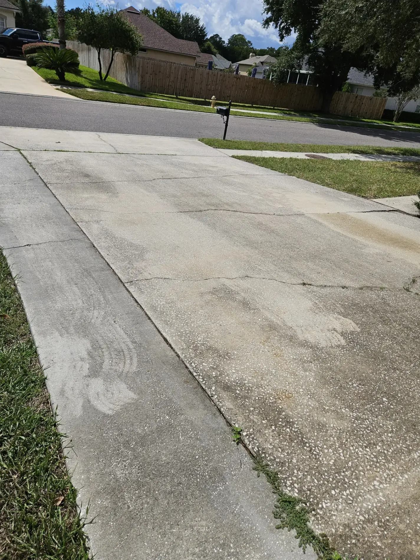 Concrete driveway in a suburban neighborhood with houses, trees, and a mailbox under a clear sky.