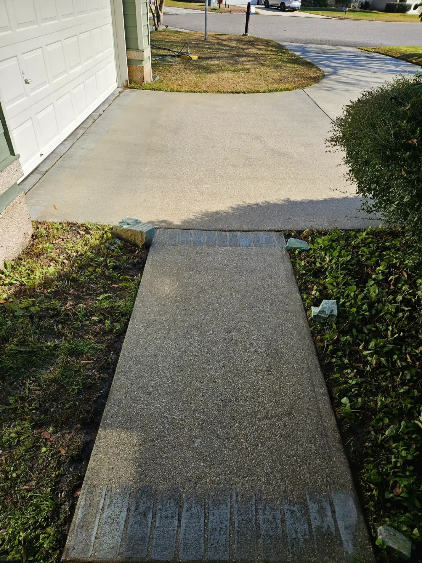 Concrete sidewalk ramp meeting a driveway, with grass and a garage on the left.