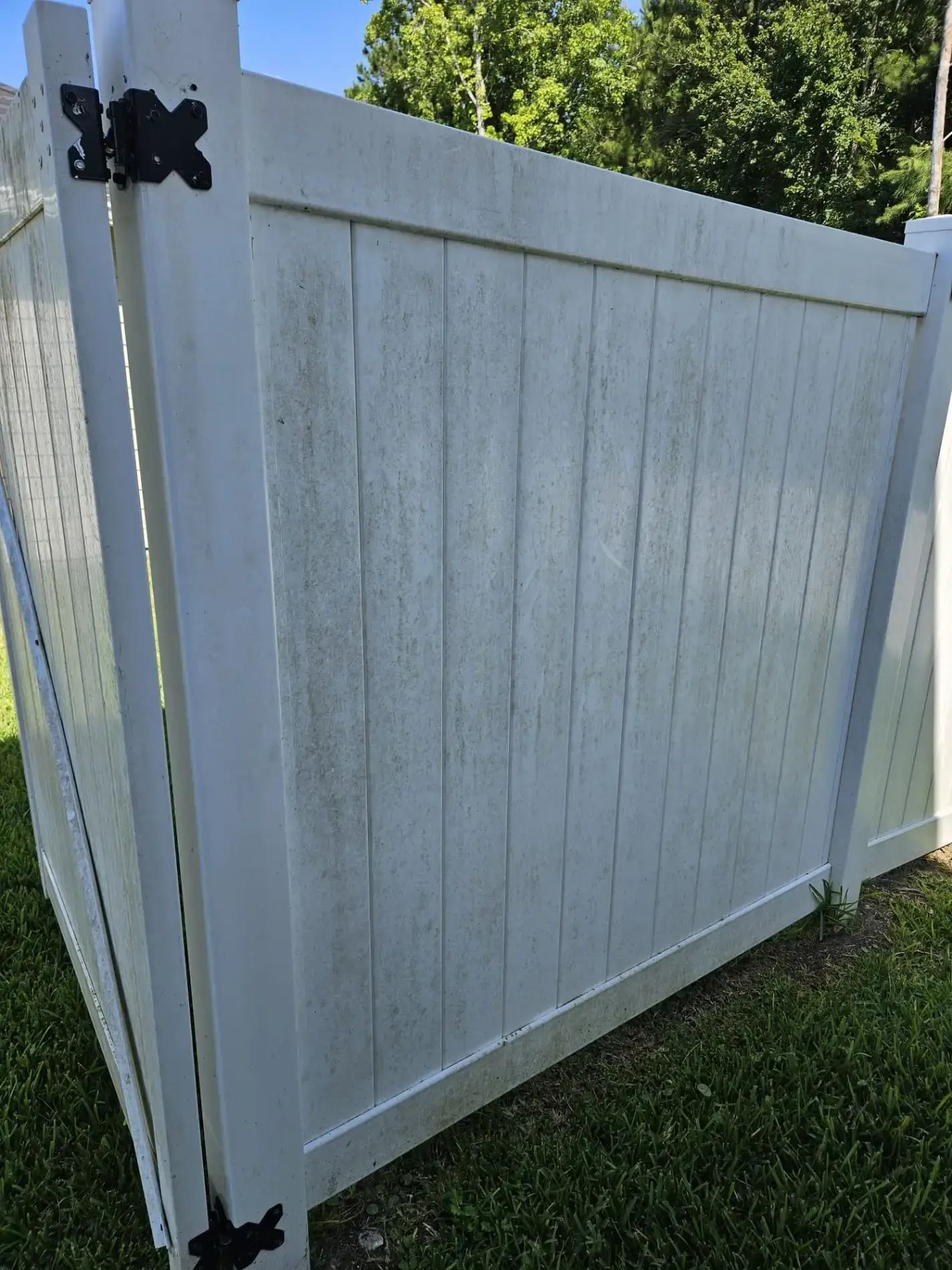 White vinyl fence gate with black hinges beside a grassy yard and trees