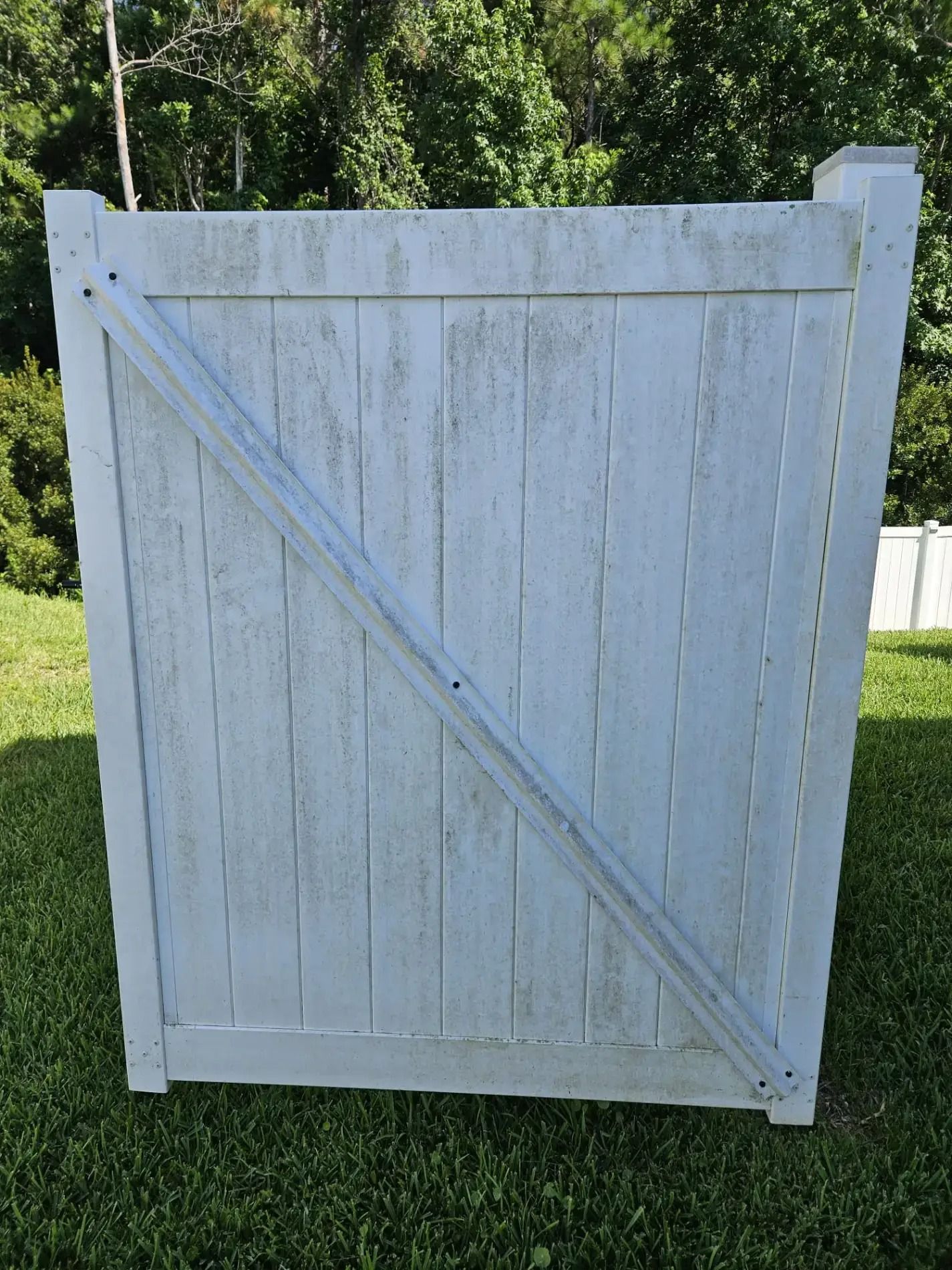 White wooden garden gate with diagonal brace standing on grass in front of trees.
