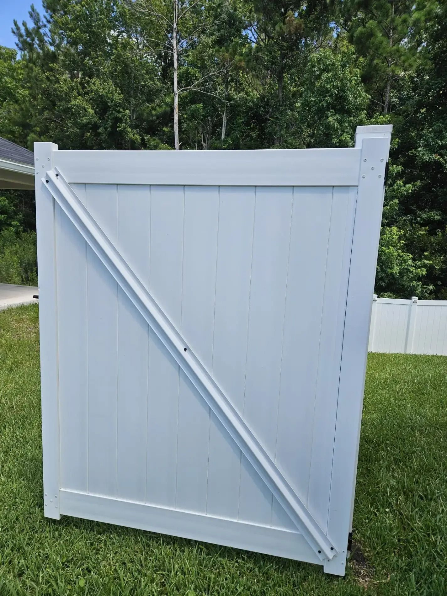 White wooden fence gate with diagonal brace, standing outdoors against green trees