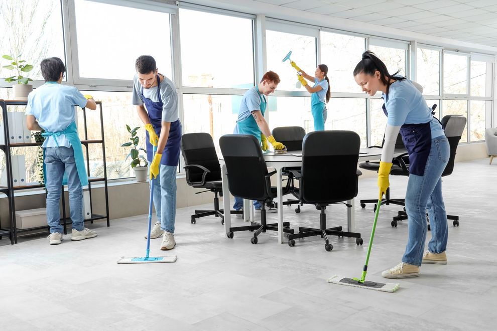 People mopping a bright office floor around desks and chairs