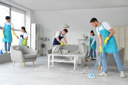 Two people cleaning a bright kitchen with spray bottles and cloths, wiping cabinets and counters
