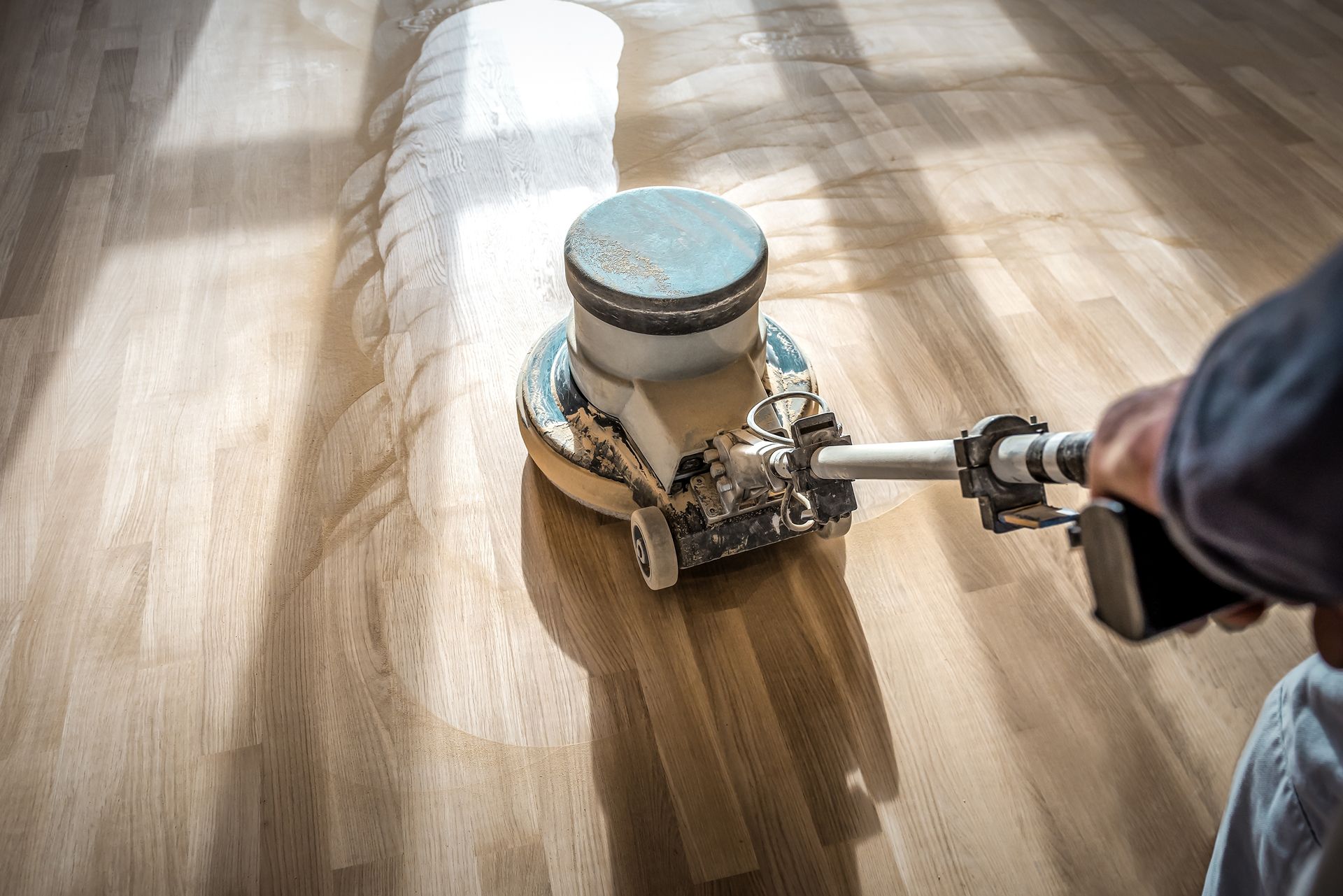 Person sanding a wooden floor with a floor sander, creating a smooth finish