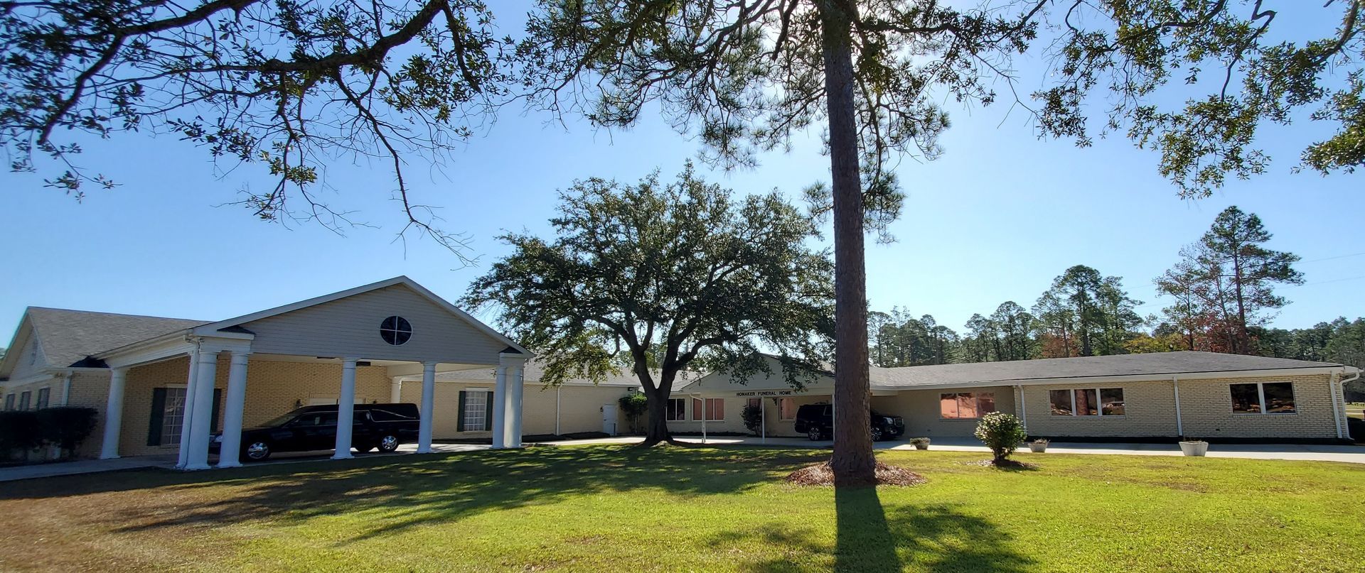 Single-story beige building with a covered entrance, trees, and grassy lawn under a blue sky