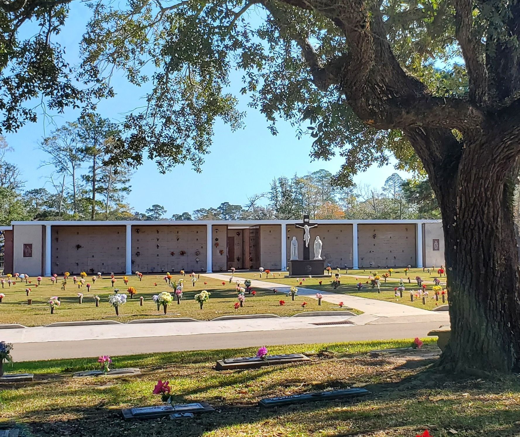 Memorial cemetery with small white grave markers under a large tree beside a brick building