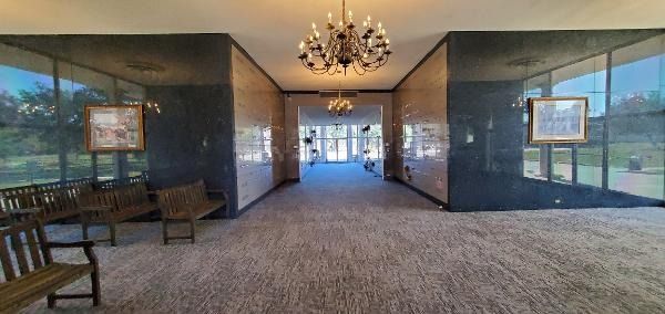 Empty hotel lobby with chandelier, benches, and glass walls opening to a bright exterior