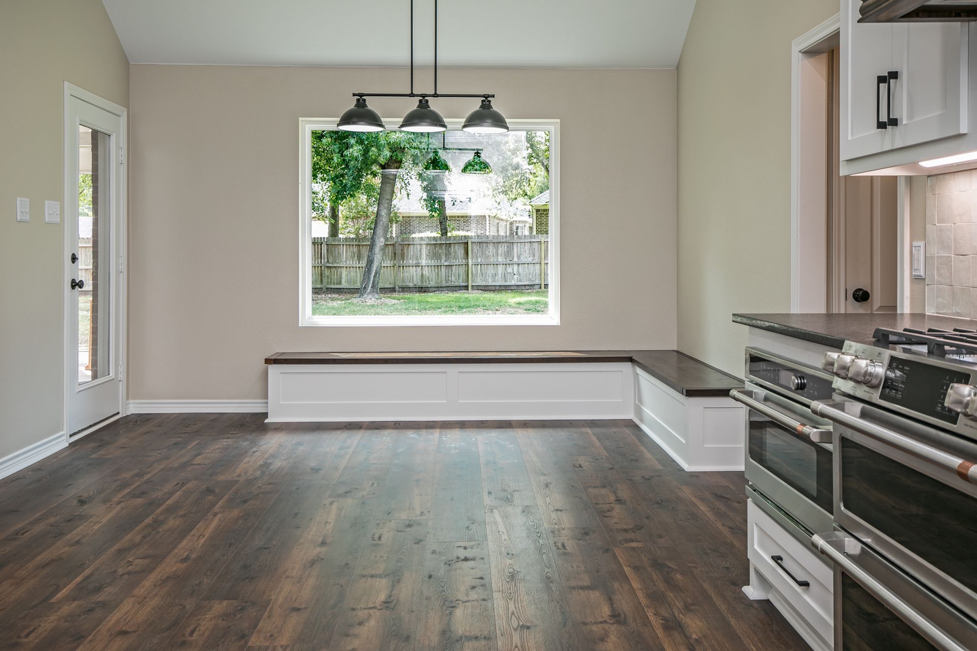 An empty kitchen with hardwood floors and a large window.