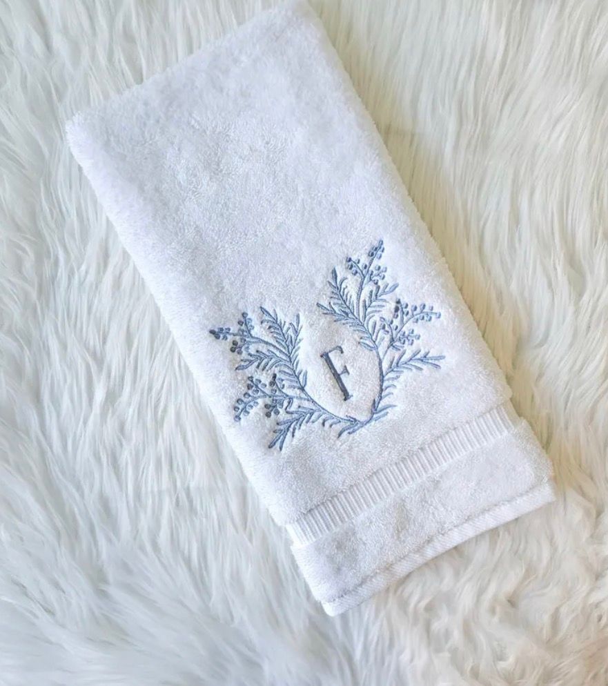 White towel with a blue embroidered floral design and the letter 