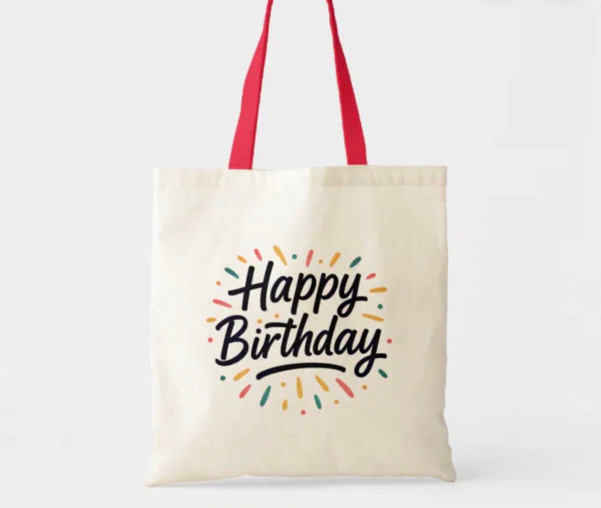 Canvas tote bag with red handles, “Happy Birthday” in black script, colorful burst design.