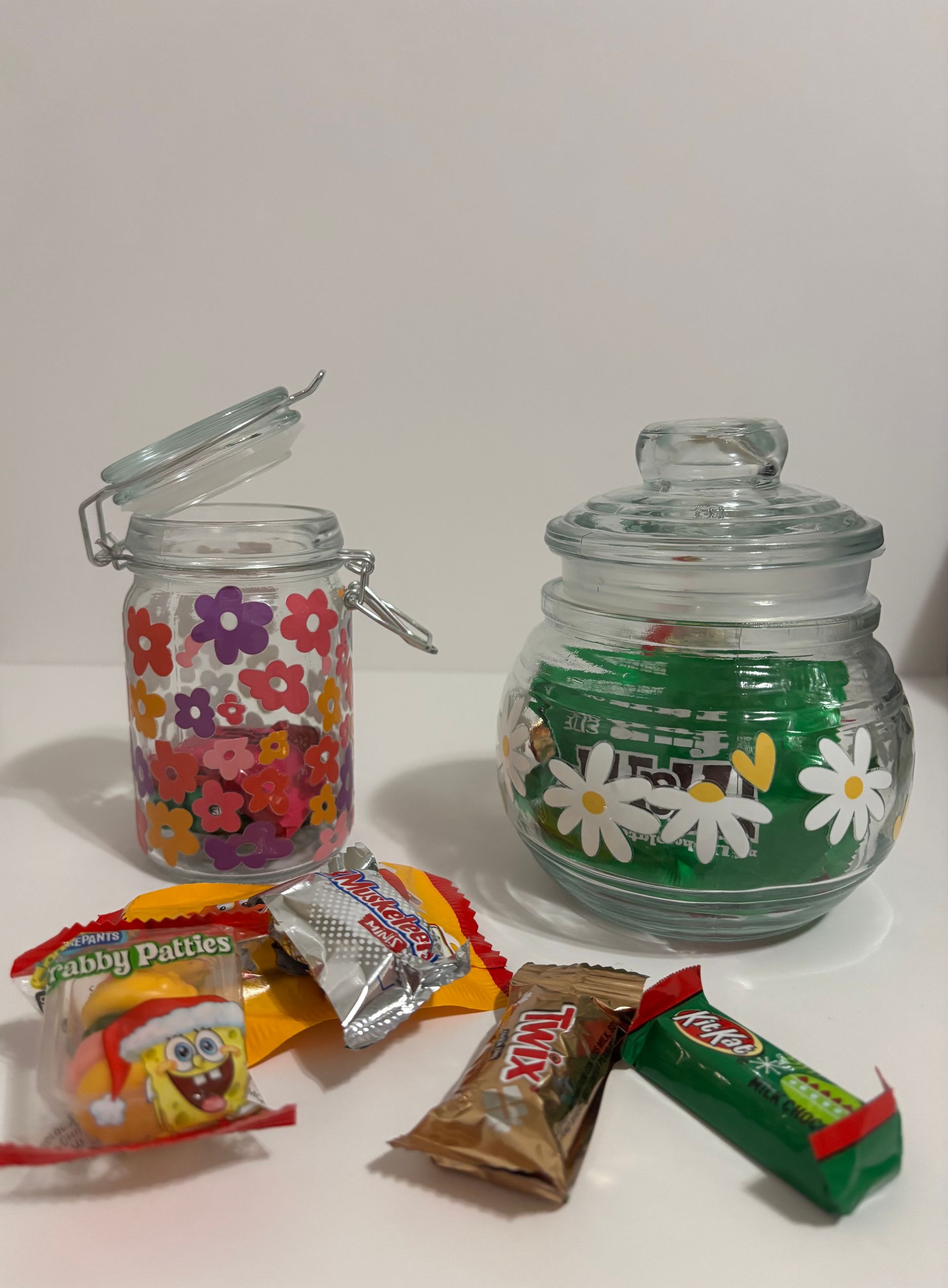 Two glass jars with candy scattered in front of them. One jar has a floral design and is open.