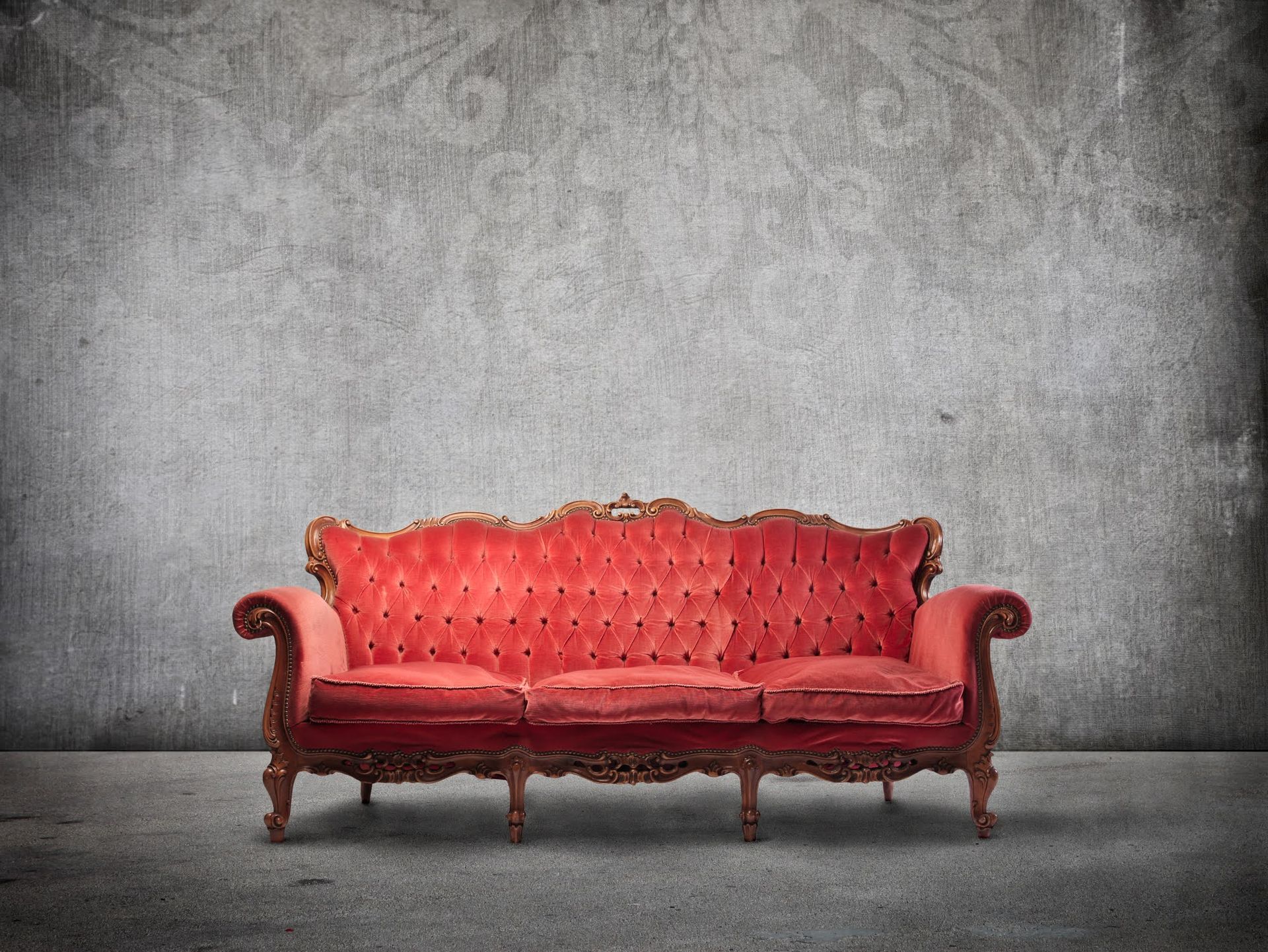 Red vintage sofa against a gray textured wall on a plain studio backdrop