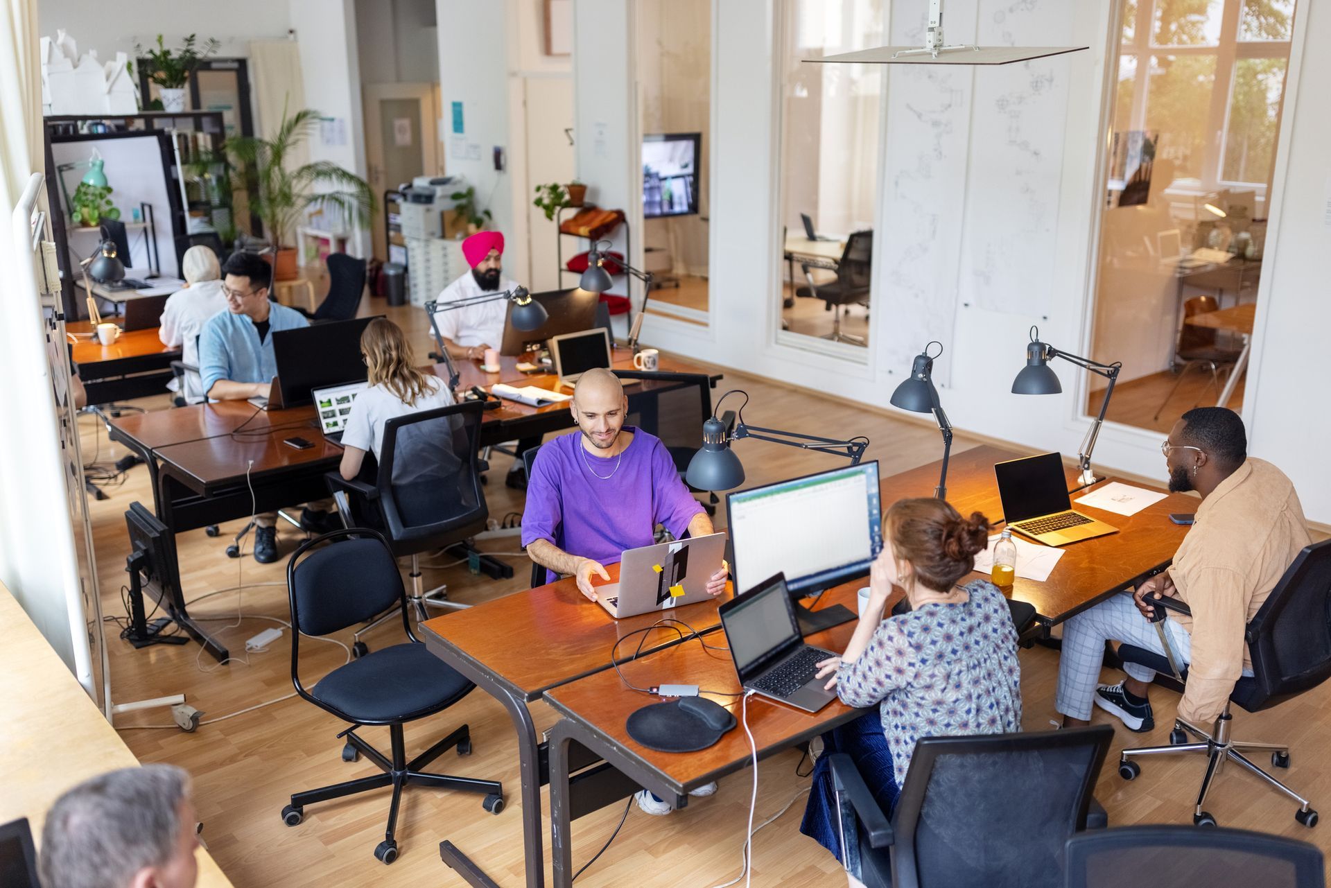 People working at desks in a bright open office with laptops and computers