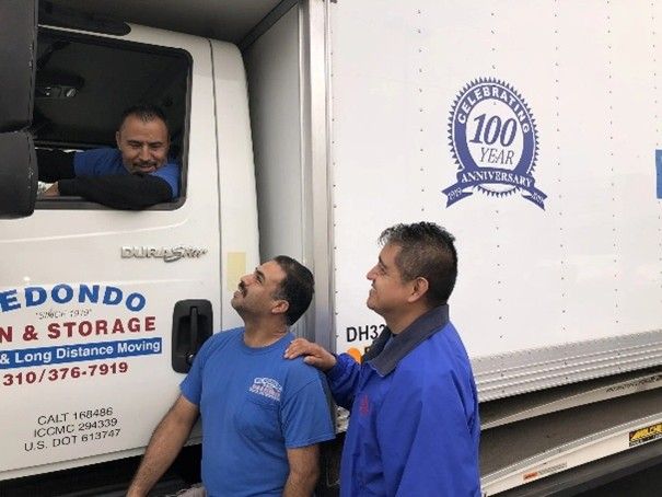 Two movers stand beside a Redondo Van & Storage moving truck, while another sits behind the wheel.